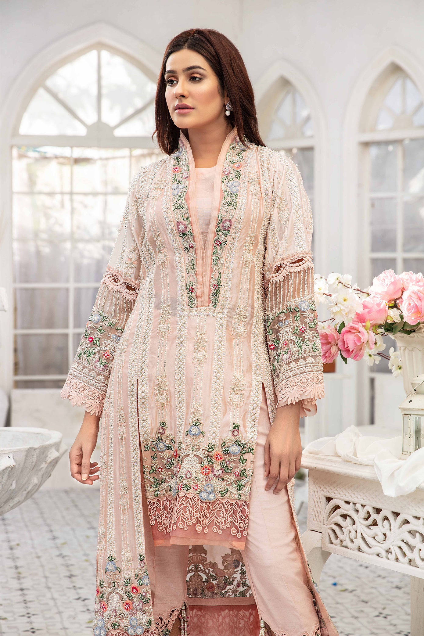 A light pink Pakistani formal dress with intricate green and red flower work embroidered on it. The dress is elegant and graceful, with flowing fabric and delicate details. The embroidery is done in a traditional style, creating a beautiful contrast against the soft pink background. The dress is perfect for formal events and special occasions.