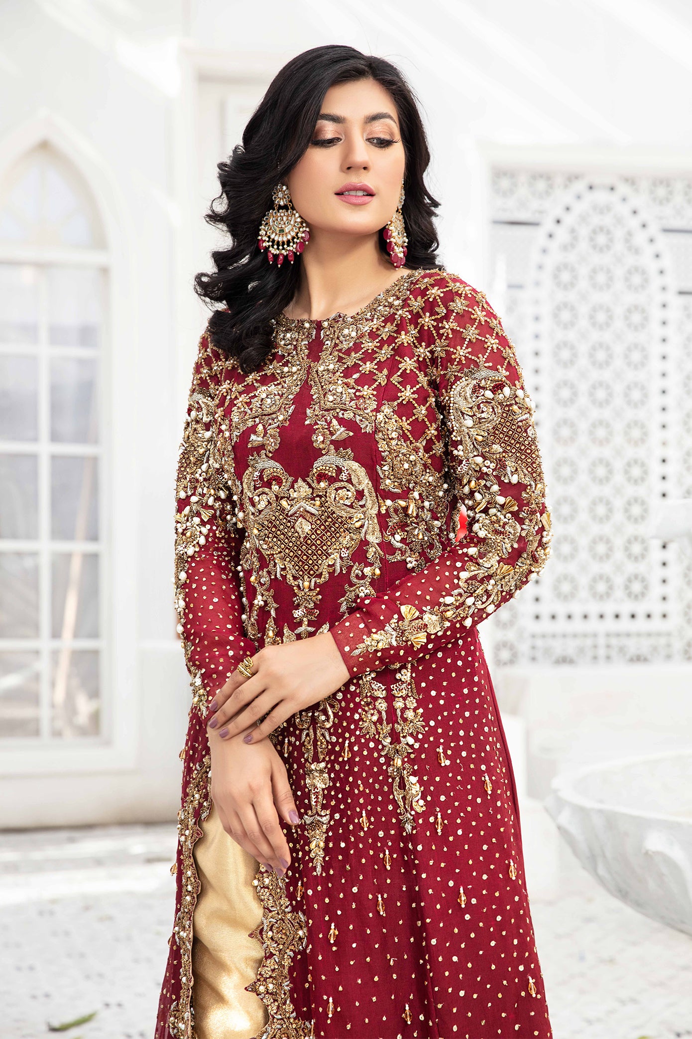 A Red and Gold Pakistani Formal Dress with intricate gold work on the sleeves, neckline, and hemline. The dress has a long flowing silhouette in a rich red color and is paired with a comfortable gold trouser with gold work on the hemline. The dress exudes elegance and sophistication, making it perfect for special occasions. The wearer is standing with a confident posture, showcasing the regal and luxurious look of the dress.
