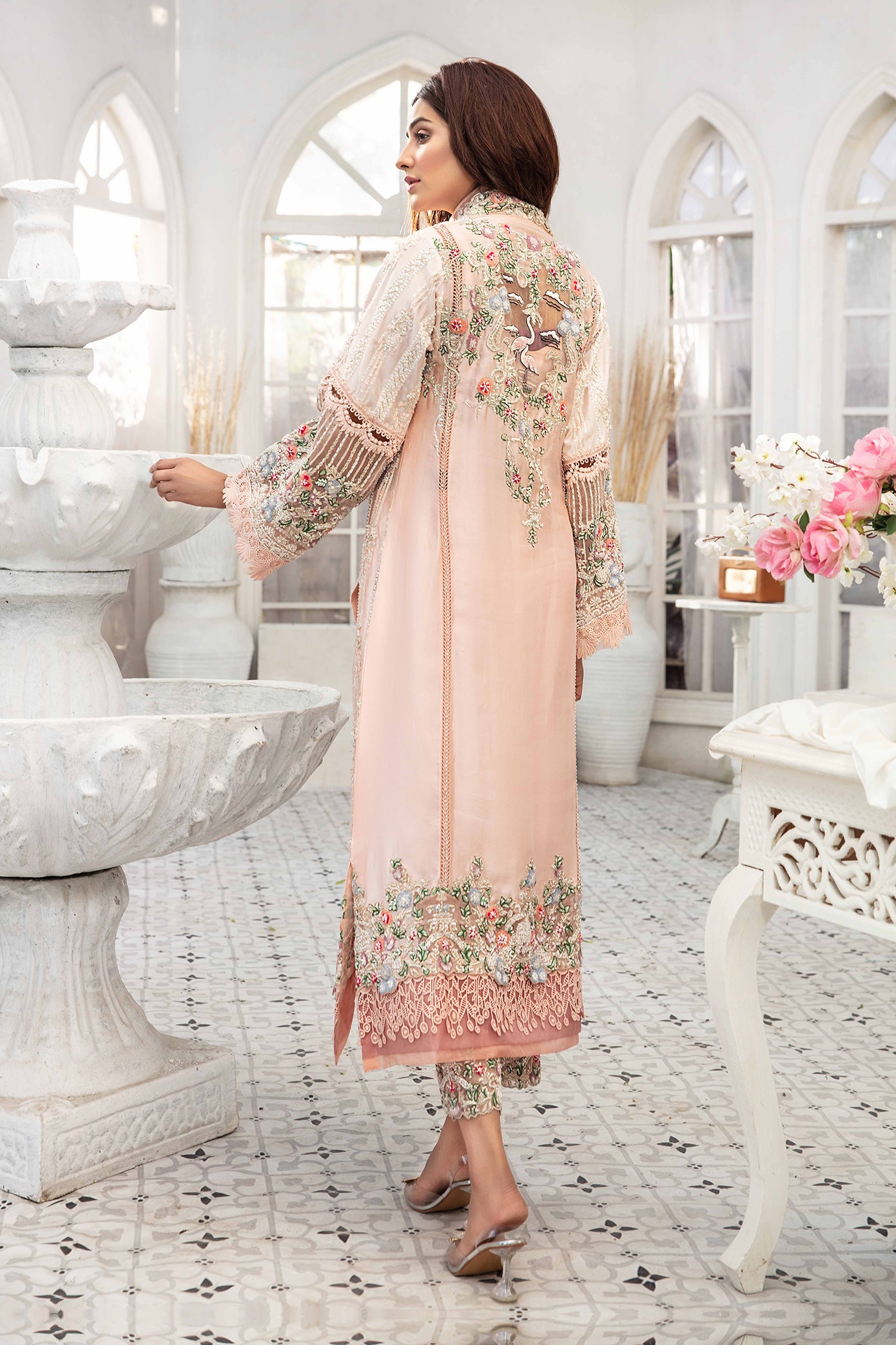 A light pink Pakistani formal dress with intricate green and red flower work embroidered on it. The dress is elegant and graceful, with flowing fabric and delicate details. The embroidery is done in a traditional style, creating a beautiful contrast against the soft pink background. The dress is perfect for formal events and special occasions.