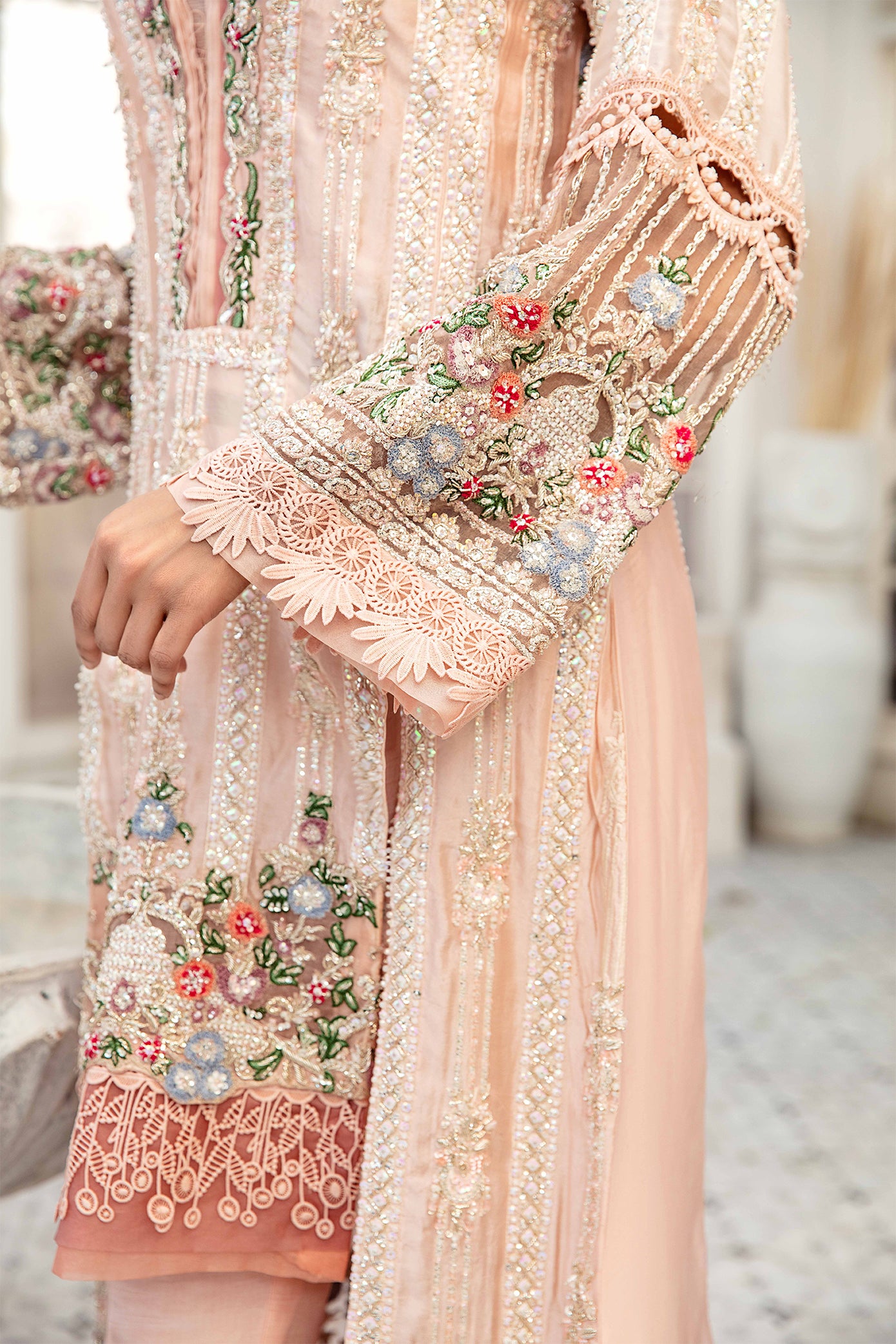 A light pink Pakistani formal dress with intricate green and red flower work embroidered on it. The dress is elegant and graceful, with flowing fabric and delicate details. The embroidery is done in a traditional style, creating a beautiful contrast against the soft pink background. The dress is perfect for formal events and special occasions.