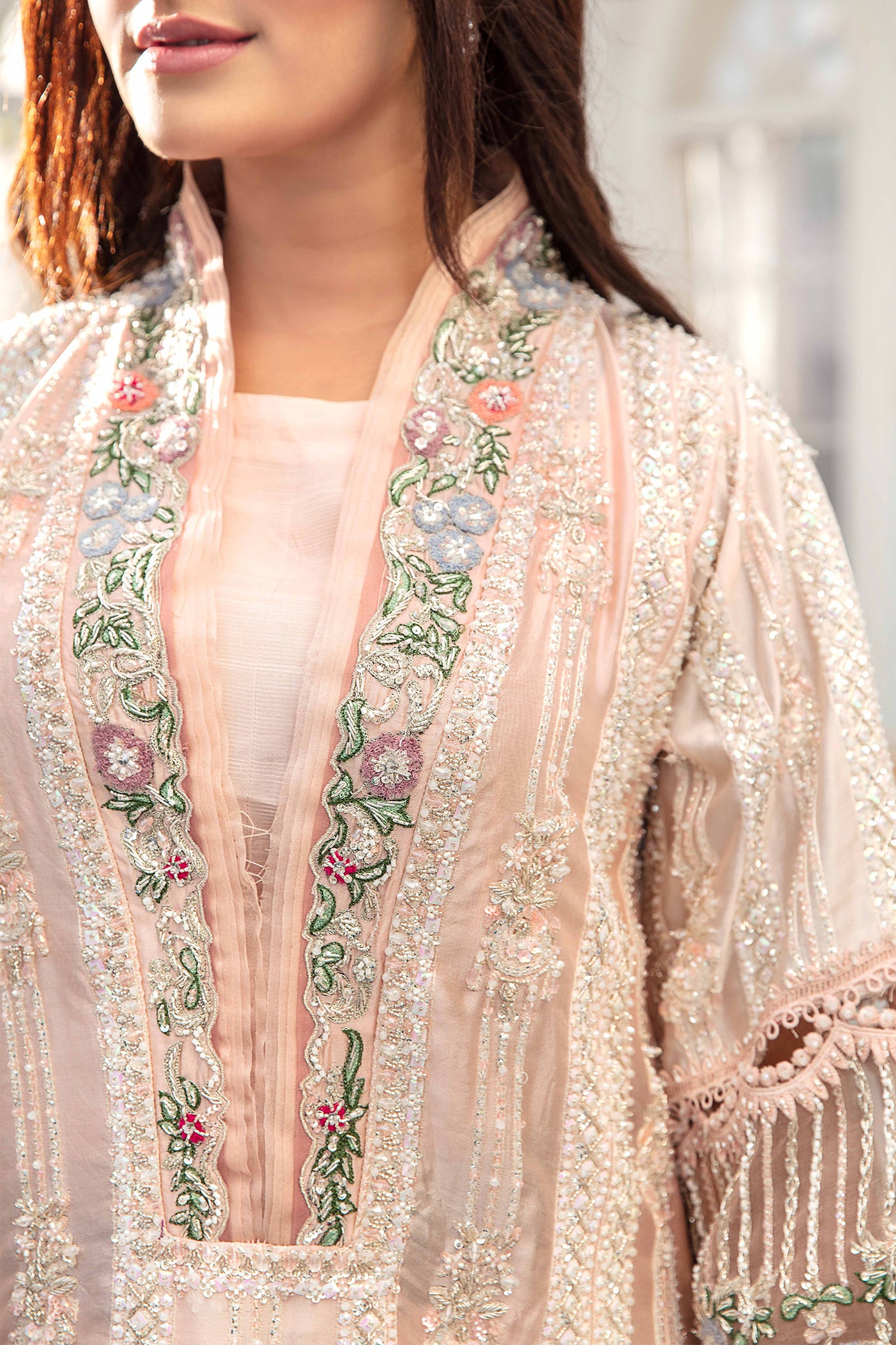 A light pink Pakistani formal dress with intricate green and red flower work embroidered on it. The dress is elegant and graceful, with flowing fabric and delicate details. The embroidery is done in a traditional style, creating a beautiful contrast against the soft pink background. The dress is perfect for formal events and special occasions.