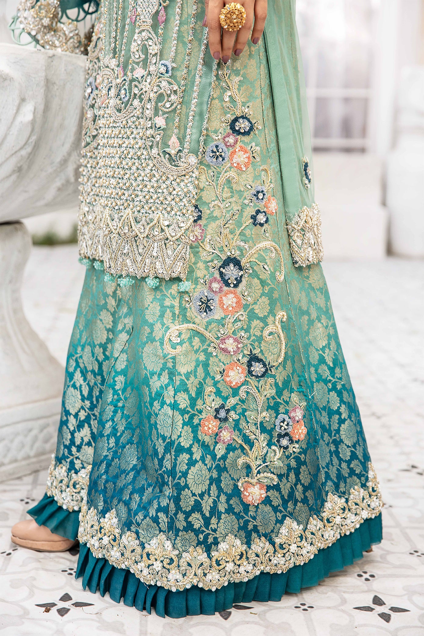 A Pakistani formal dress with green and blue tones, intricate silver work on the main body, and delicate pink work on the arms. It comes with a matching dubatta featuring silver work on the borders and center, crafted with traditional Pakistani embroidery techniques.