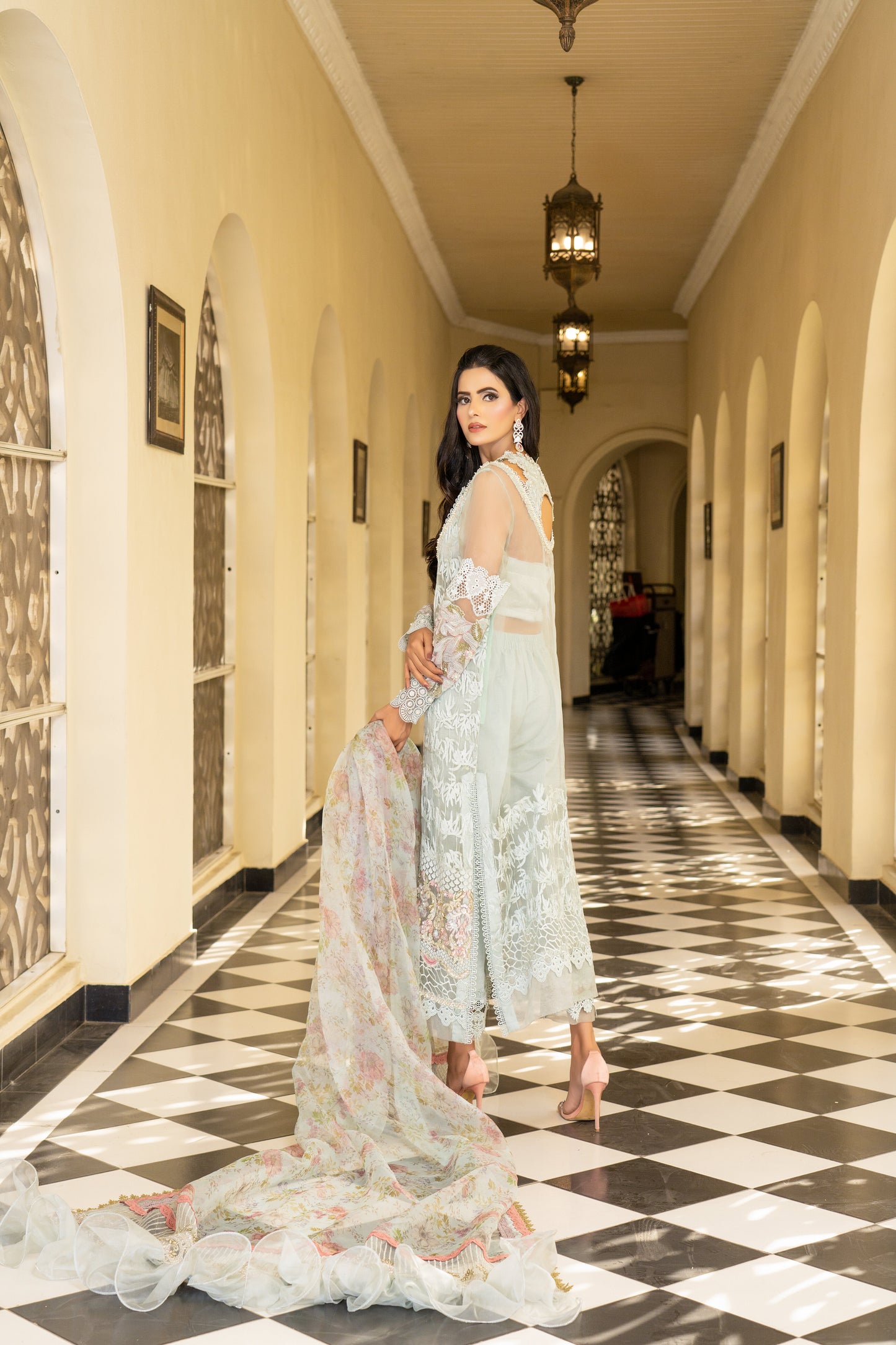 A Pakistani luxury Pret outfit consisting of a white shirt with intricate embroidery work, featuring pink fabric work at the bottom. The outfit is paired with a pink and white dupatta with flower prints.