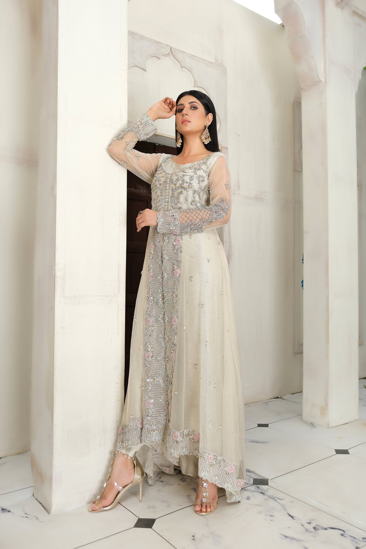 light nude Pakistani formal dress with intricate silver work. The dress features delicate embroidery, sequins, and other hand-crafted designs that create a unique and beautiful pattern on the fabric. It has a long, flowing silhouette that drapes beautifully on the body and full-length sleeves with silver work detailing. The neckline is also adorned with silver work embellishments, adding glamour and sophistication to the dress.