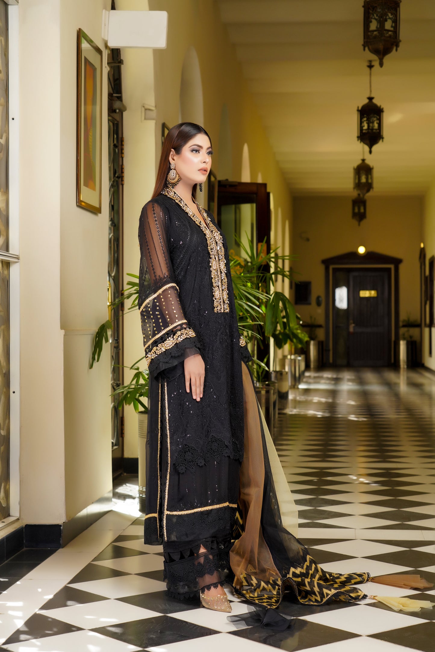 Luxurious black and gold Pakistani dress with intricate gold work around neckline and sleeves. Flattering fitted bodice and flowing skirt. Elegant v-neckline and long sleeves with stunning gold embroidery. Perfect for special occasions exuding confidence, power, and sophistication.