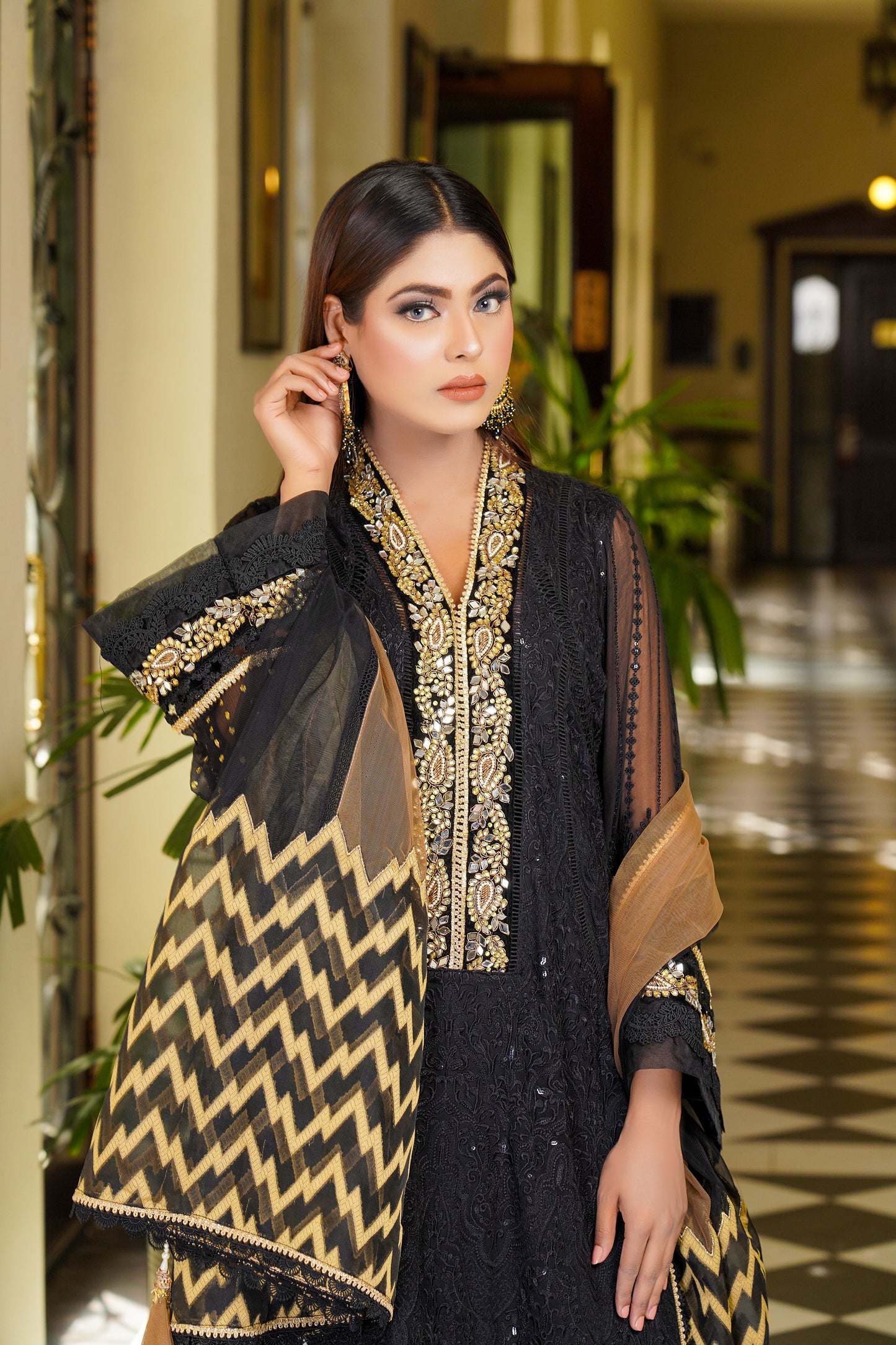 Luxurious black and gold Pakistani dress with intricate gold work around neckline and sleeves. Flattering fitted bodice and flowing skirt. Elegant v-neckline and long sleeves with stunning gold embroidery. Perfect for special occasions exuding confidence, power, and sophistication.