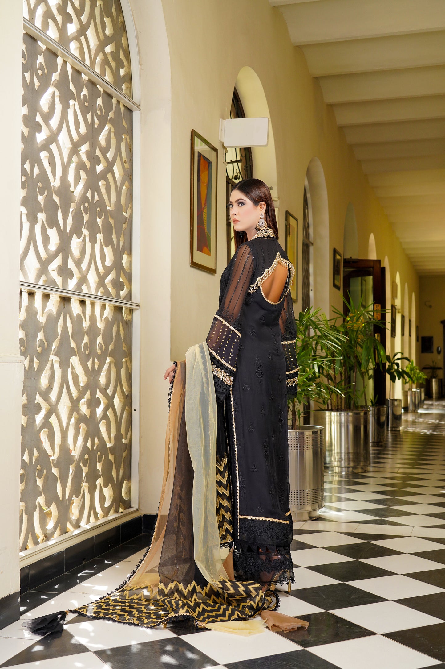 Luxurious black and gold Pakistani dress with intricate gold work around neckline and sleeves. Flattering fitted bodice and flowing skirt. Elegant v-neckline and long sleeves with stunning gold embroidery. Perfect for special occasions exuding confidence, power, and sophistication.