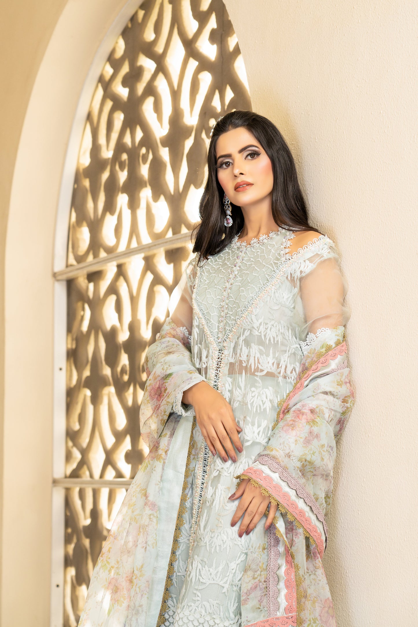 A Pakistani luxury Pret outfit consisting of a white shirt with intricate embroidery work, featuring pink fabric work at the bottom. The outfit is paired with a pink and white dupatta with flower prints.