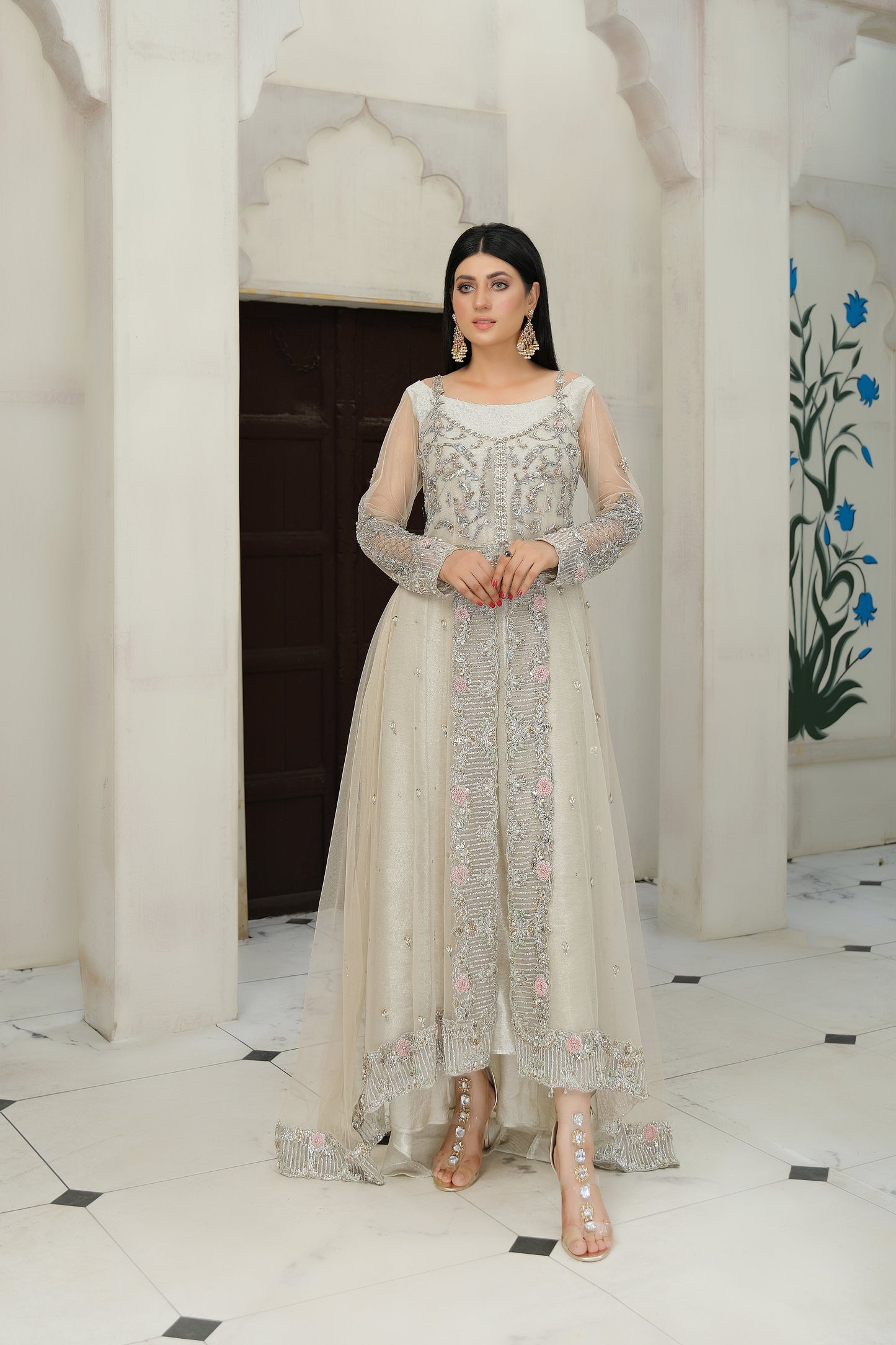 light nude Pakistani formal dress with intricate silver work. The dress features delicate embroidery, sequins, and other hand-crafted designs that create a unique and beautiful pattern on the fabric. It has a long, flowing silhouette that drapes beautifully on the body and full-length sleeves with silver work detailing. The neckline is also adorned with silver work embellishments, adding glamour and sophistication to the dress.