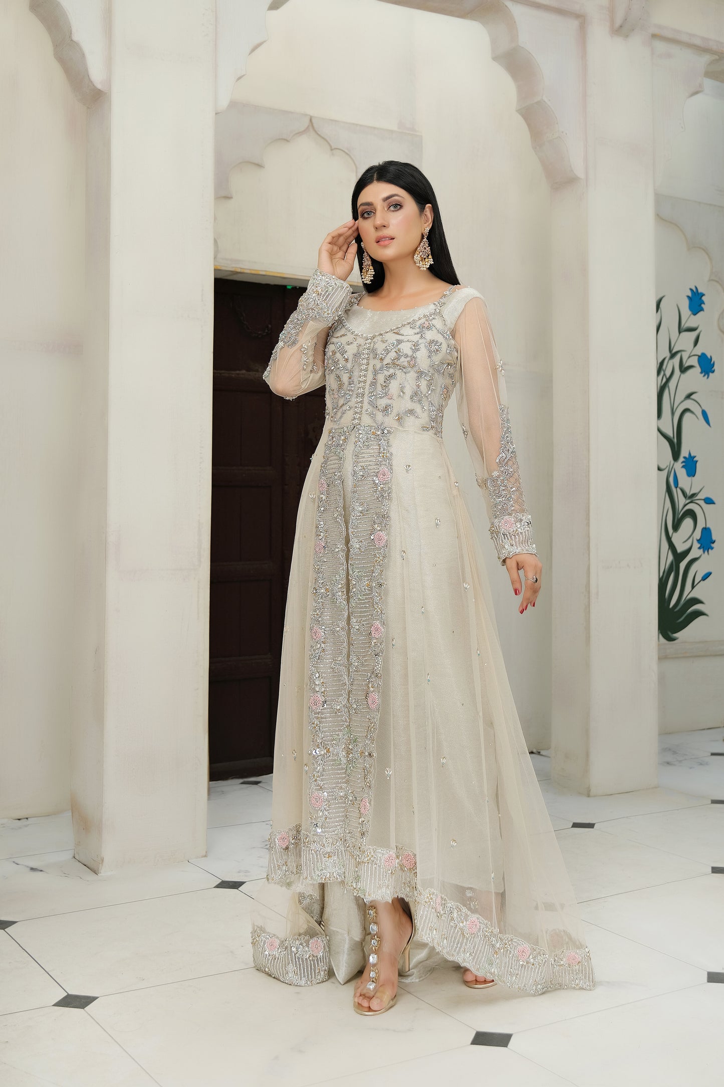 light nude Pakistani formal dress with intricate silver work. The dress features delicate embroidery, sequins, and other hand-crafted designs that create a unique and beautiful pattern on the fabric. It has a long, flowing silhouette that drapes beautifully on the body and full-length sleeves with silver work detailing. The neckline is also adorned with silver work embellishments, adding glamour and sophistication to the dress.