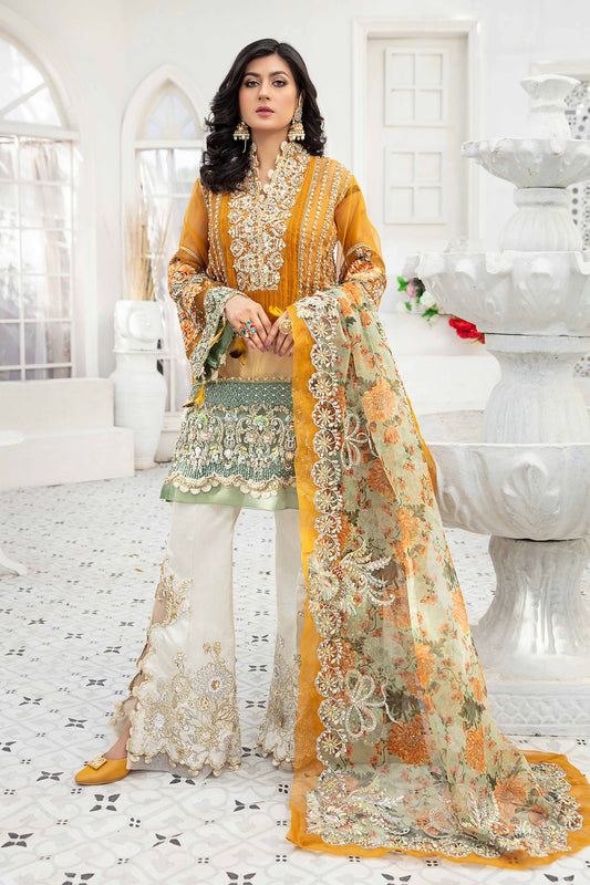 A Pakistani formal dress ensemble featuring a mustard-colored, long flowing gown made of luxurious materials such as silk or chiffon. The gown is adorned with intricate silver work on the neckline, sleeves, and hemline. The model is wearing off-white trousers that complement the gown's color. A printed organza dupatta with delicate floral or geometric designs is draped over the model's head and shoulders, adding a touch of whimsy to the overall look.