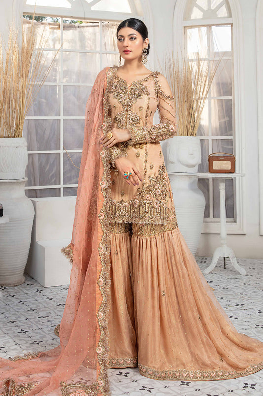 A Peach Gold Pakistani Bridal Dress with intricate gold work on the bodice, sleeves, and hemline. The dress has a fitted silhouette and is made of high-quality fabric that drapes beautifully. The dress is paired with a soft pink chiffon dupatta with intricate gold work on its borders. The bride is standing with a veil draped over her head, looking elegant and regal.