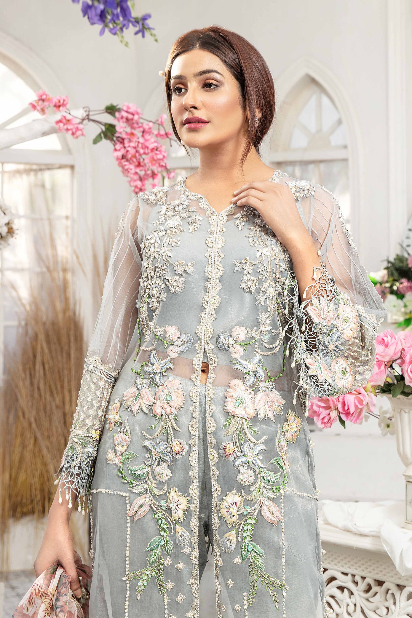 Grey and peach Pakistani formal dress with printed organza on the dupatta. The dress has a grey or silver toned base with intricate peach-colored embroidery or embellishments. The scarf or dupatta is made of light and sheer organza fabric with a delicate print.