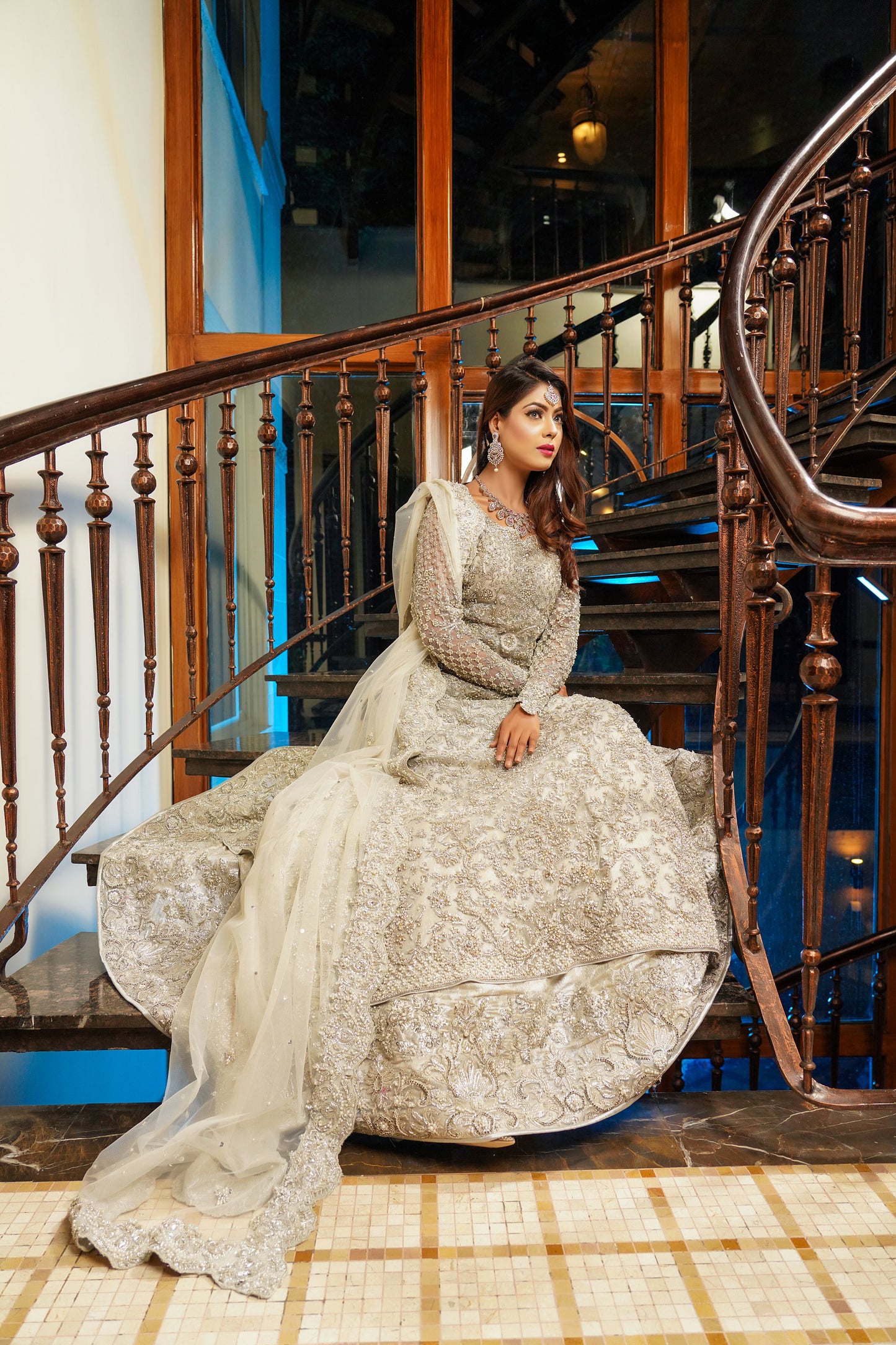 Silver and grey Pakistani bridal dress. The dress features intricate silver work embellishments on a soft grey fabric, creating an elegant and sophisticated look. The fitted bodice has silver embroidery and beadwork, while the flowing skirt has a heavy silver border. The outfit comes with a matching dupatta that complements the dress with delicate silver work details. 