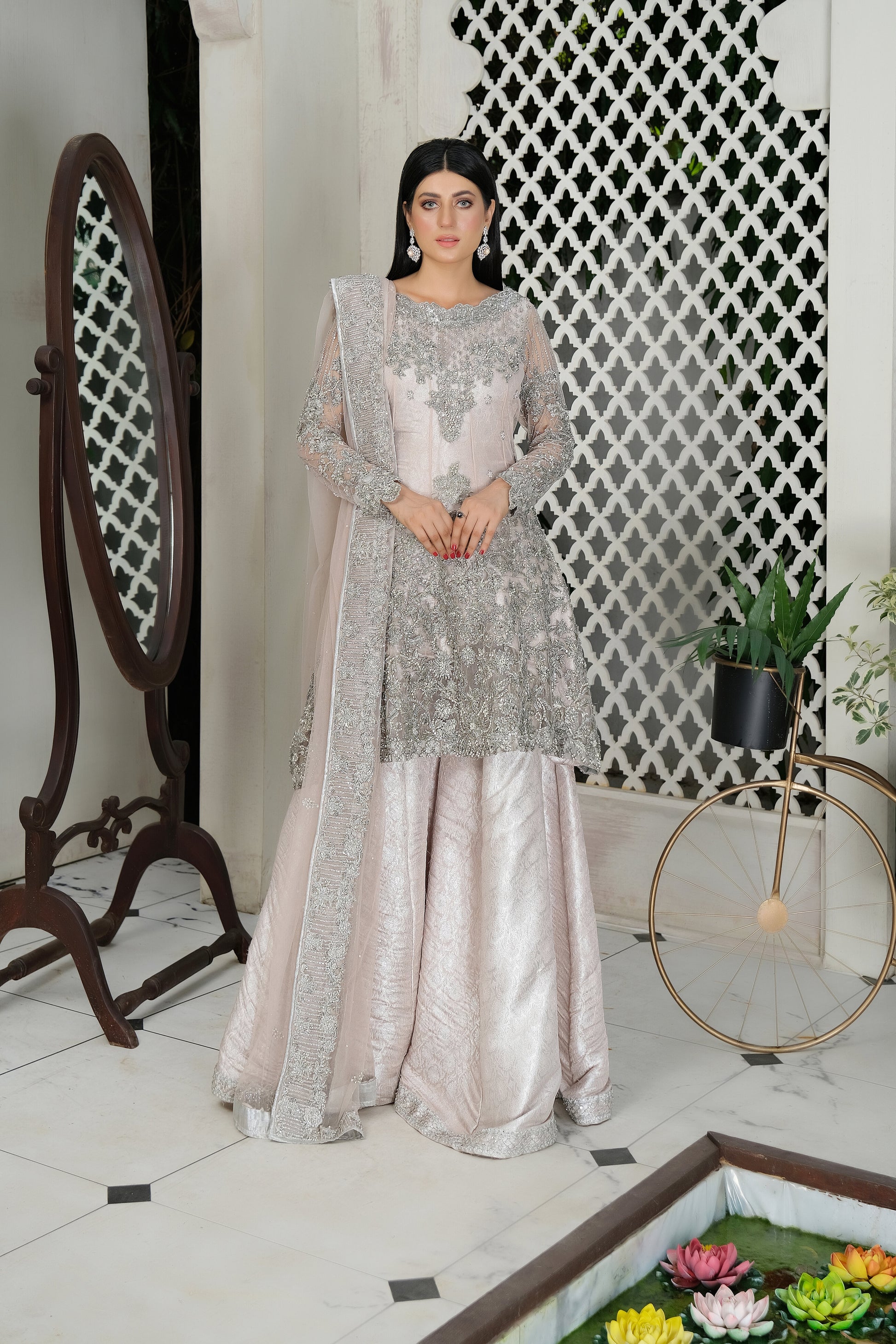 A beautiful blend of soft pink fabric and intricate silver embroidery, creating a striking contrast. The dress is elegantly adorned with silver details that flow seamlessly down the length of the dress, with a matching dupatta that adds an extra layer of grace. Perfect for any formal occasion, this dress is sure to impress with its delicate and eye catching design