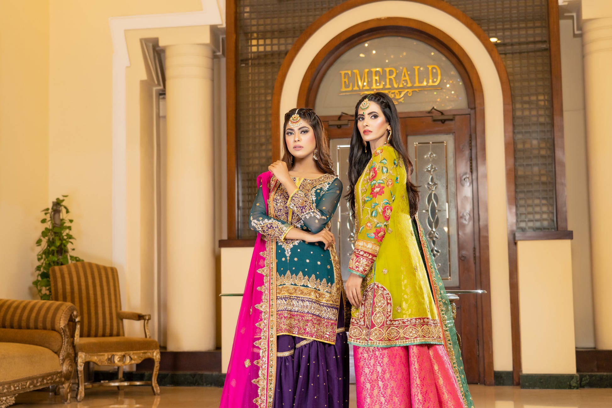 A stunning Pakistani bridal dress in yellow and pink with a green dupatta. Intricate gold handwork with embroidery, sequins, and beadwork in floral and paisley patterns. Fitted bodice with a sweetheart neckline and long sleeves, and a flowing skirt with a wide flare. The matching dupatta is draped over the head, adding a regal touch. Perfect for brides who want to make a bold and vibrant statement.