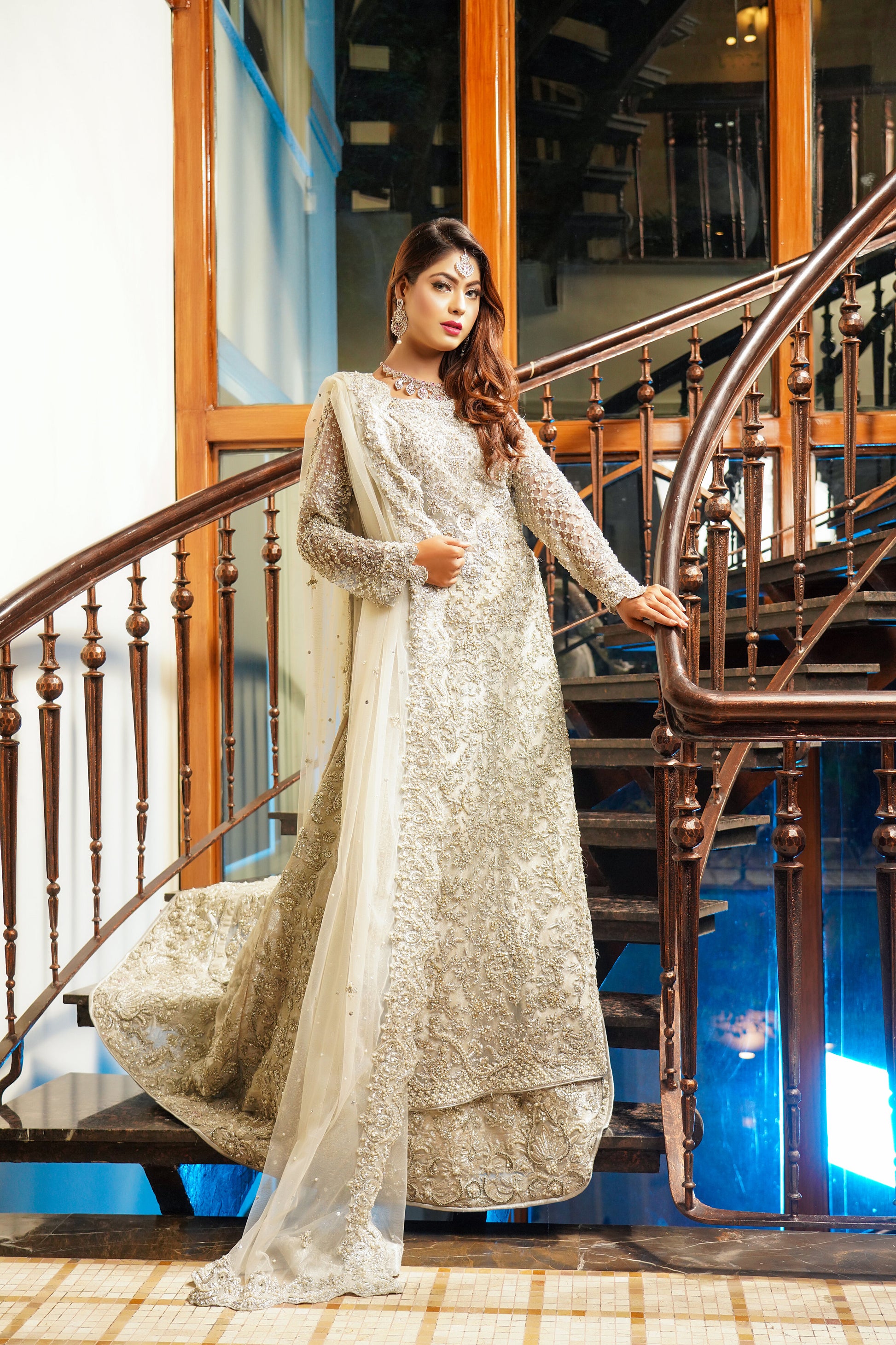 Silver and grey Pakistani bridal dress. The dress features intricate silver work embellishments on a soft grey fabric, creating an elegant and sophisticated look. The fitted bodice has silver embroidery and beadwork, while the flowing skirt has a heavy silver border. The outfit comes with a matching dupatta that complements the dress with delicate silver work details. 