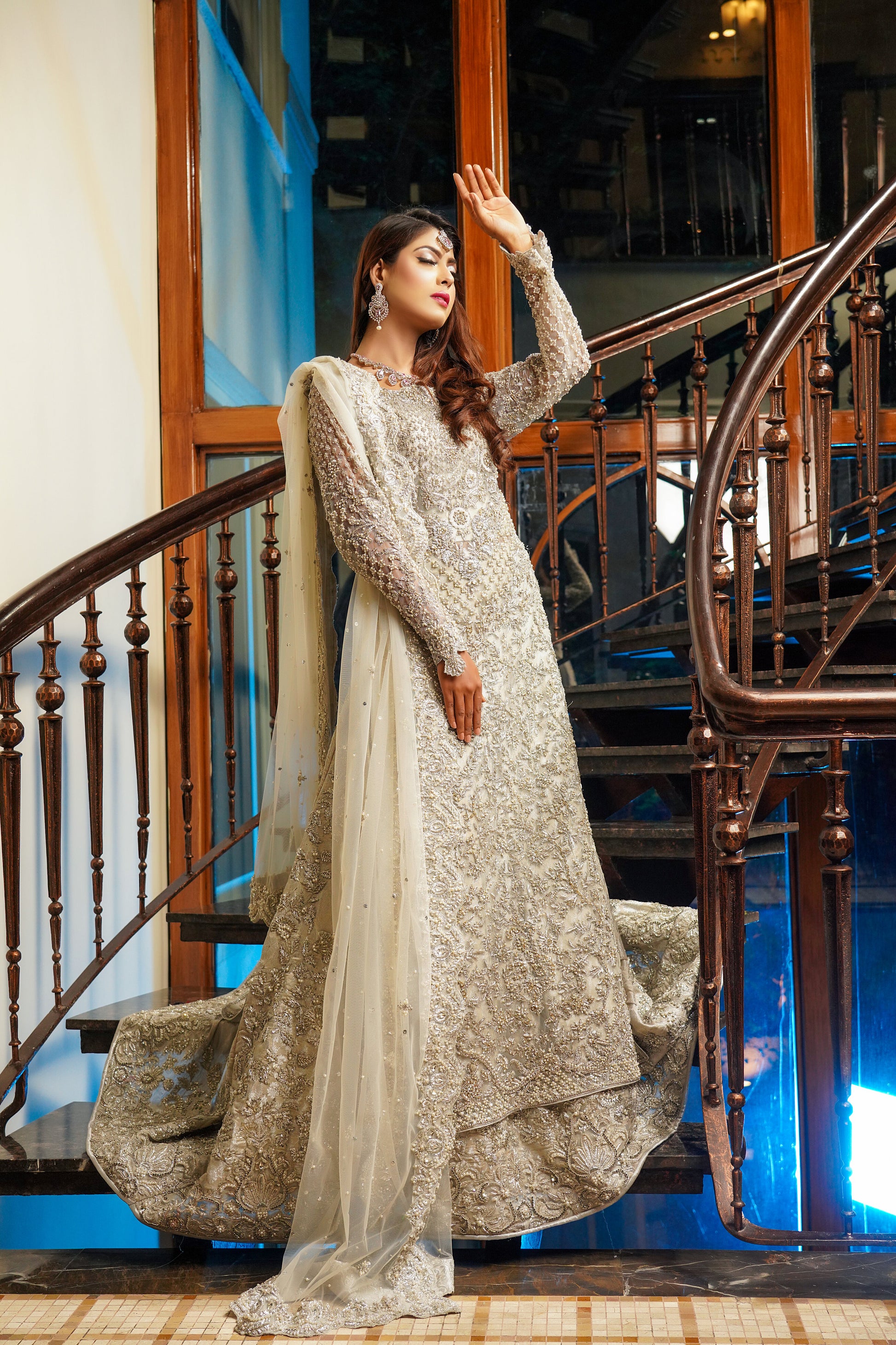 Silver and grey Pakistani bridal dress. The dress features intricate silver work embellishments on a soft grey fabric, creating an elegant and sophisticated look. The fitted bodice has silver embroidery and beadwork, while the flowing skirt has a heavy silver border. The outfit comes with a matching dupatta that complements the dress with delicate silver work details. 