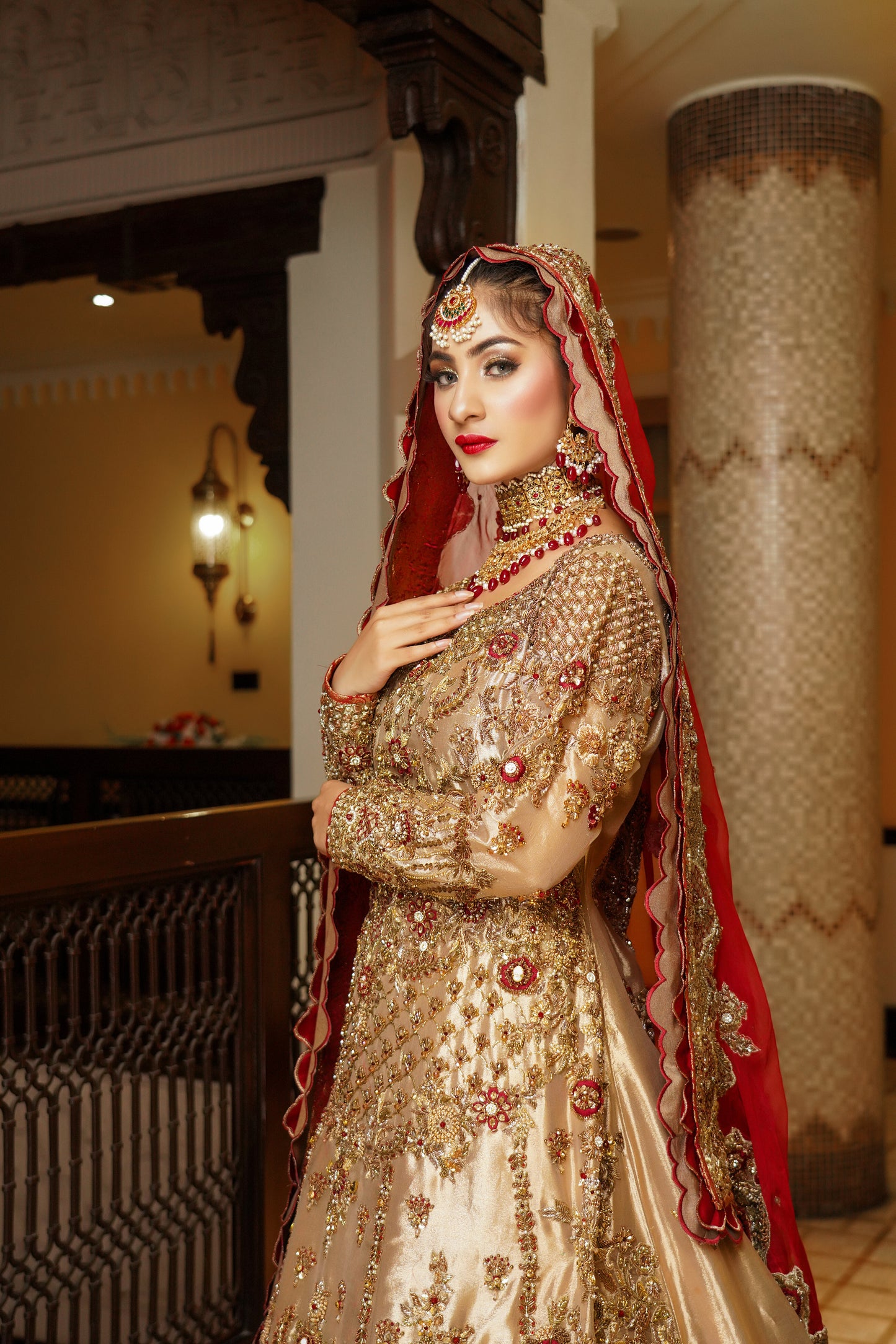 Pakistani dress with red dupatta. Predominantly gold with intricate gold work embellishments, heavy gold border with touch of red on skirt. Fitted bodice with flared skirt. Matching red dupatta with delicate gold border. Traditional and elegant outfit with a touch of color for brides.