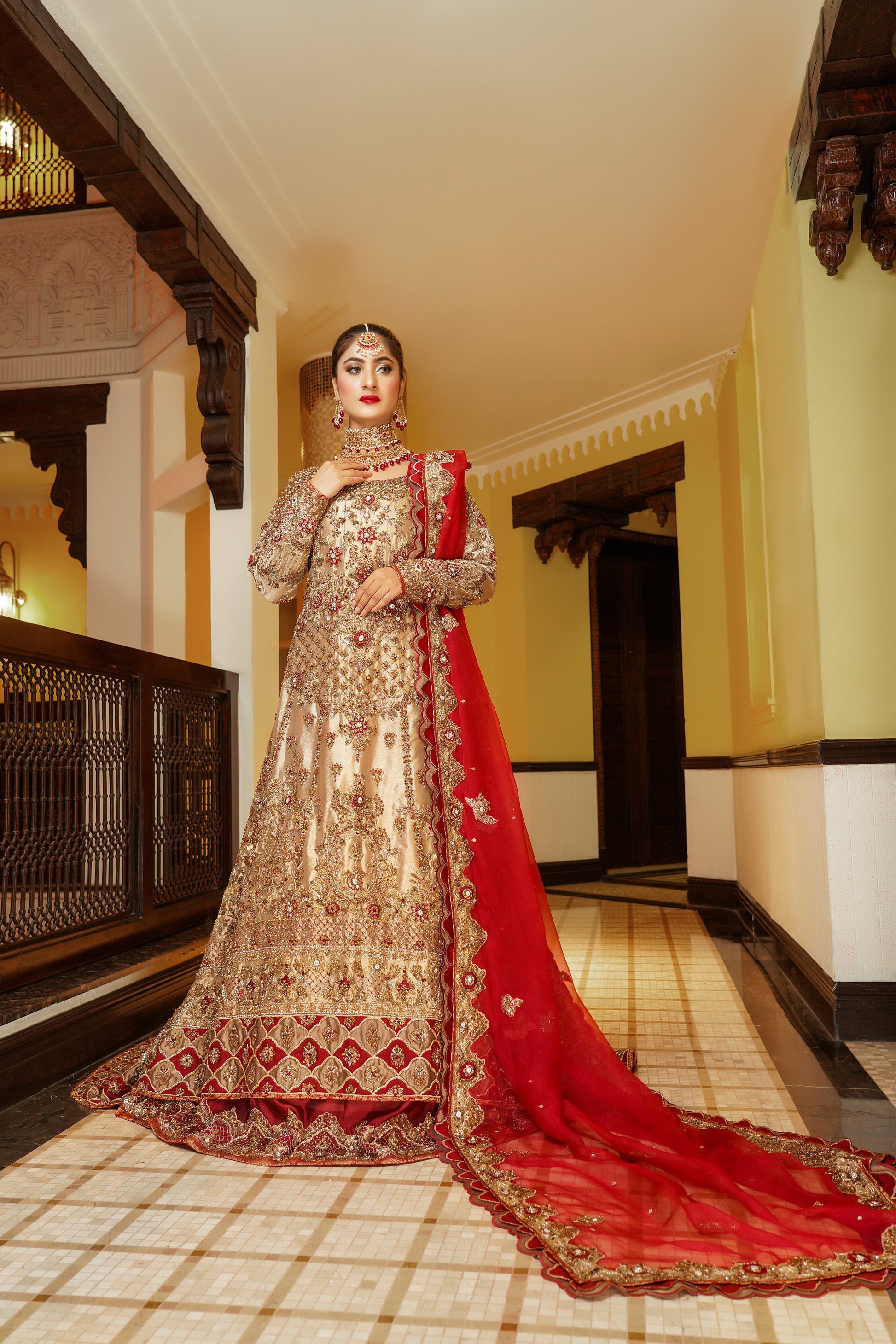 Pakistani dress with red dupatta. Predominantly gold with intricate gold work embellishments, heavy gold border with touch of red on skirt. Fitted bodice with flared skirt. Matching red dupatta with delicate gold border. Traditional and elegant outfit with a touch of color for brides.