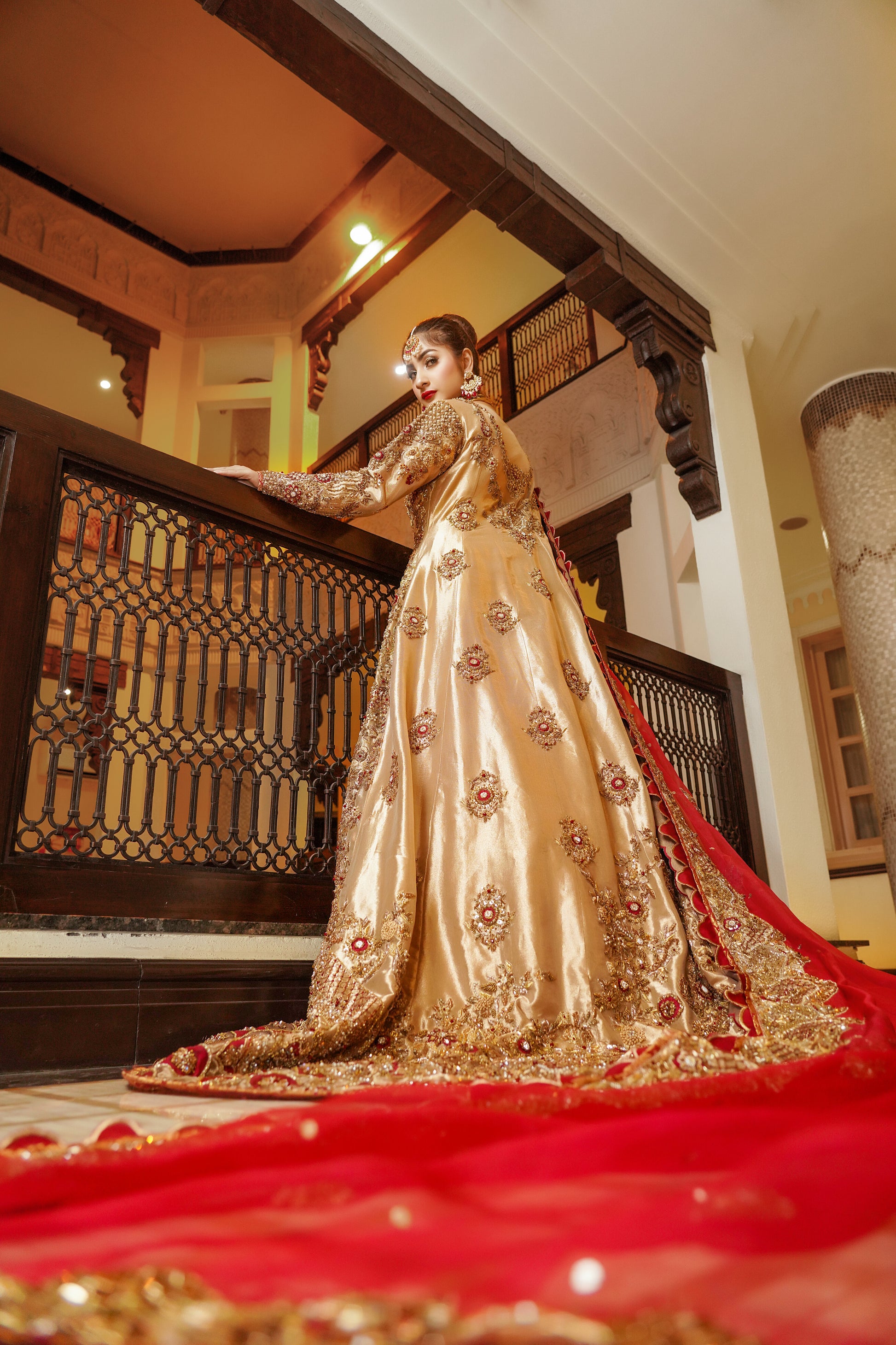 Pakistani dress with red dupatta. Predominantly gold with intricate gold work embellishments, heavy gold border with touch of red on skirt. Fitted bodice with flared skirt. Matching red dupatta with delicate gold border. Traditional and elegant outfit with a touch of color for brides.