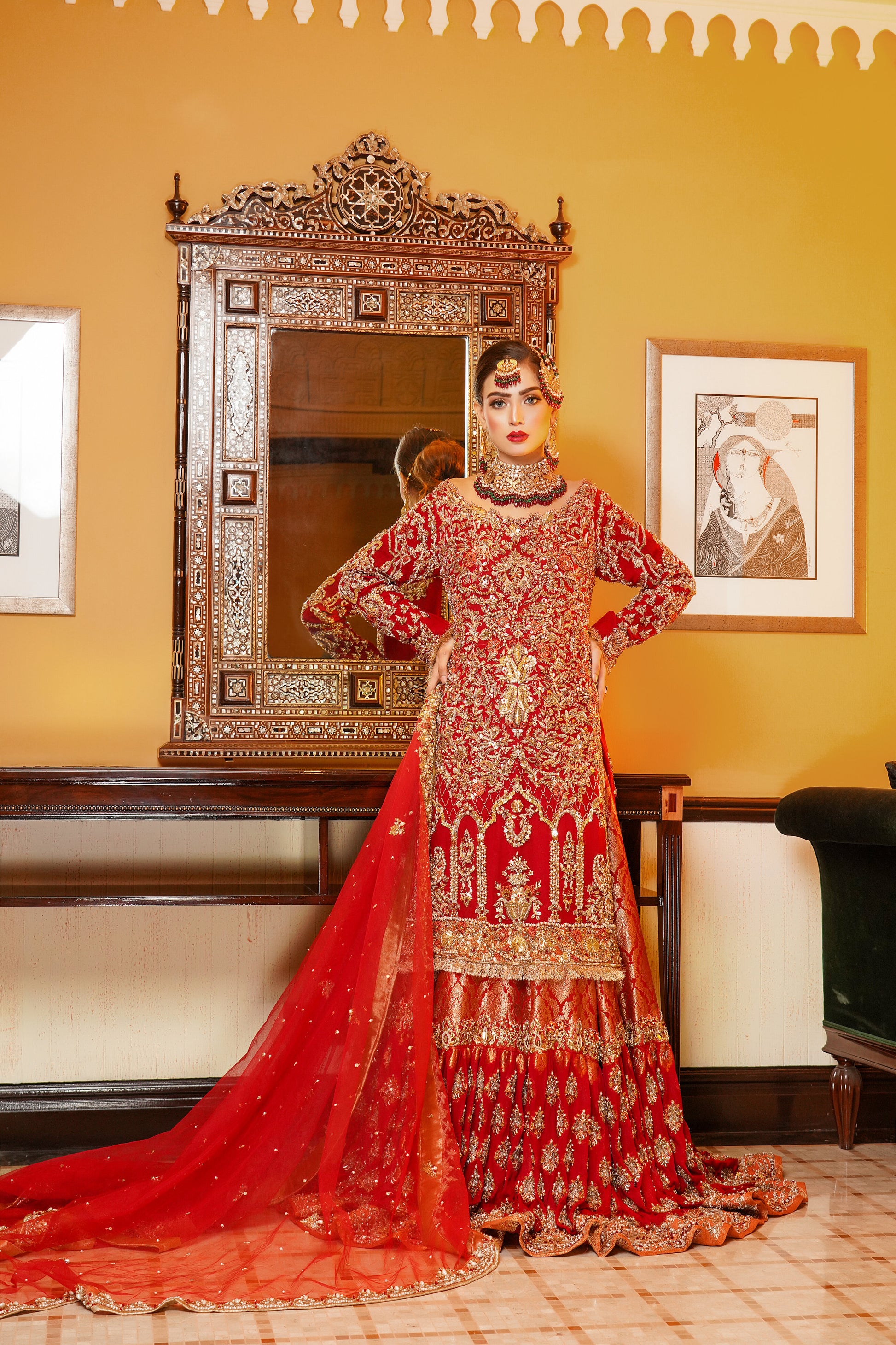 Red and gold Pakistani bridal dress. The dress is a beautiful combination of vibrant red and rich gold. The bodice of the dress features intricate gold embroidery and beadwork, while the skirt is adorned with a heavy gold border. The dress has a fitted bodice with a flared skirt that flows gracefully. The outfit is completed with a matching red dupatta that is embellished with gold embroidery. 