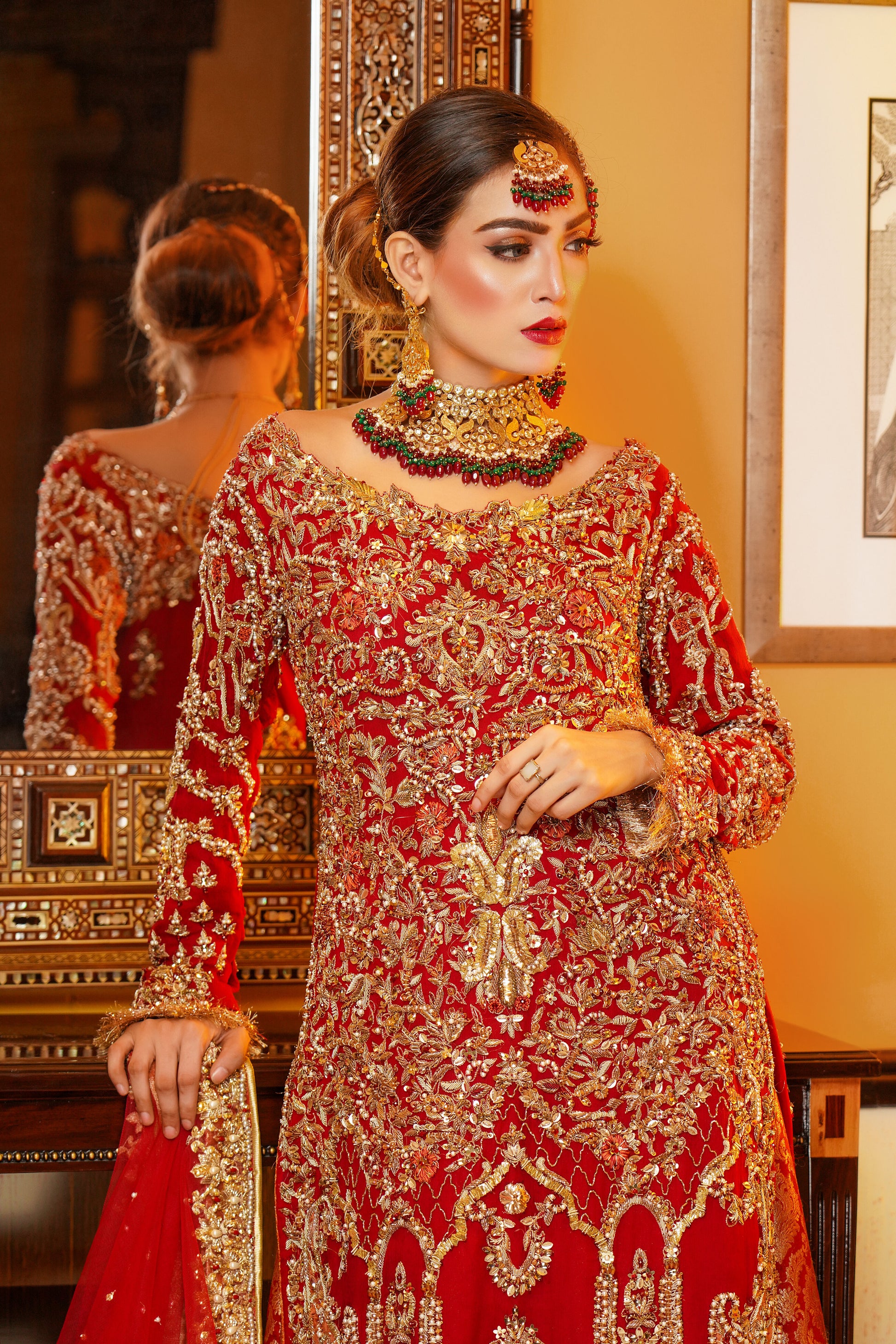 Red and gold Pakistani bridal dress. The dress is a beautiful combination of vibrant red and rich gold. The bodice of the dress features intricate gold embroidery and beadwork, while the skirt is adorned with a heavy gold border. The dress has a fitted bodice with a flared skirt that flows gracefully. The outfit is completed with a matching red dupatta that is embellished with gold embroidery. 