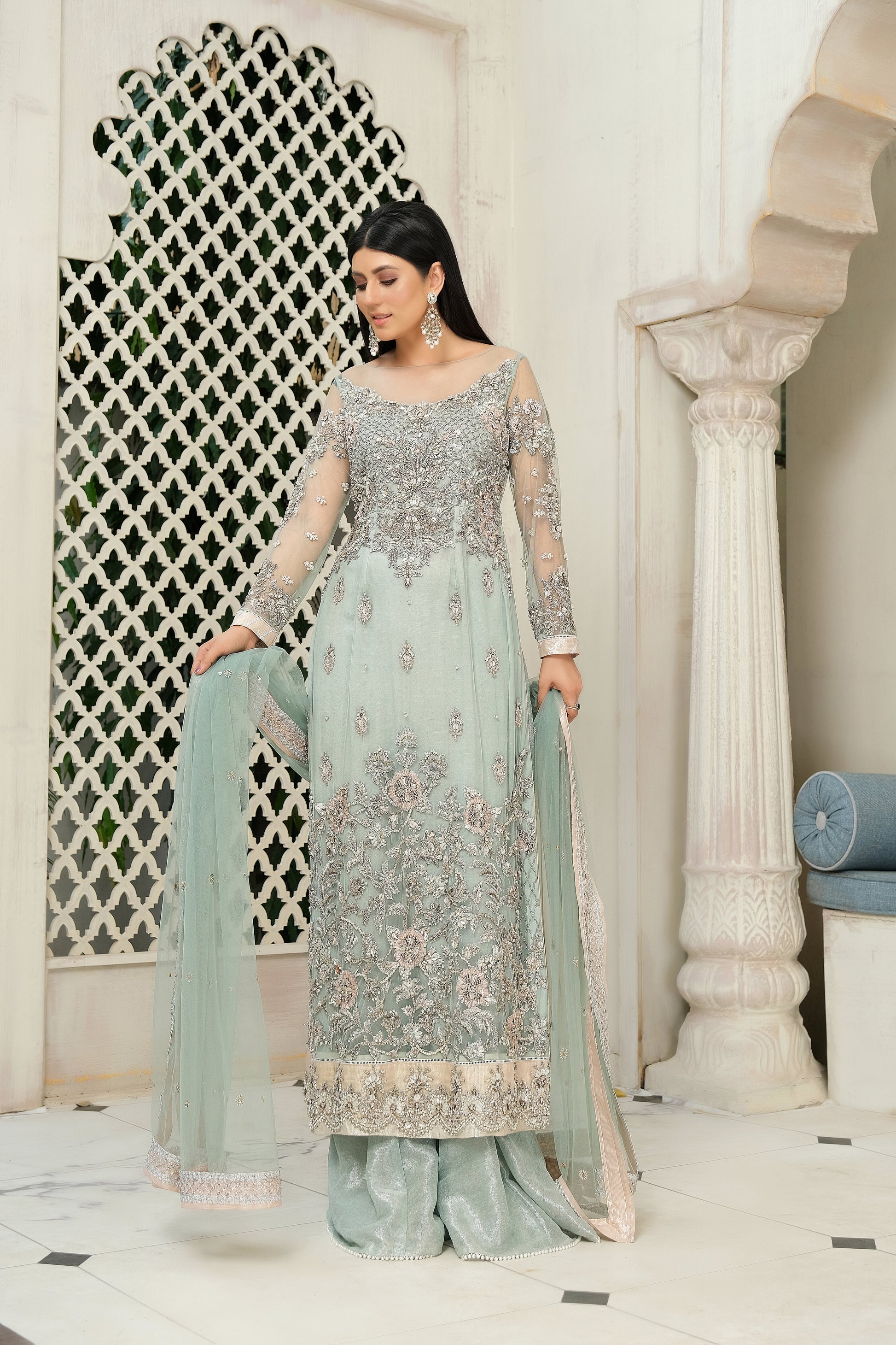 A stunning combination of blue and silver embroidery on a flowing bridal gown. The intricate silver work adorns the bodice and cascades down to the hemline, while the blue fabric provides a beautiful backdrop. The dress also features a flowing dupatta with delicate silver details, completing the elegant bridal look.