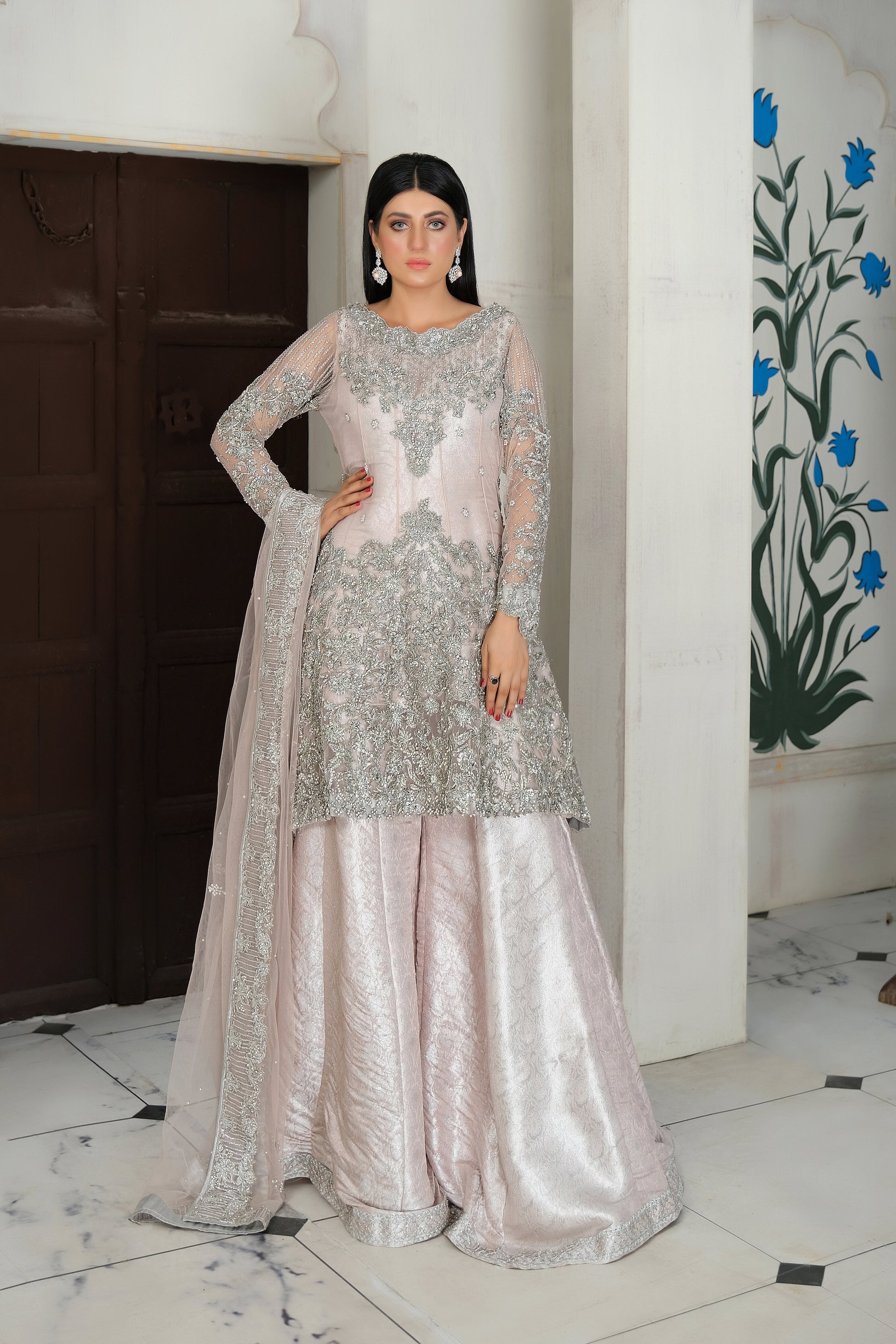 A beautiful blend of soft pink fabric and intricate silver embroidery, creating a striking contrast. The dress is elegantly adorned with silver details that flow seamlessly down the length of the dress, with a matching dupatta that adds an extra layer of grace. Perfect for any formal occasion, this dress is sure to impress with its delicate and eye catching design