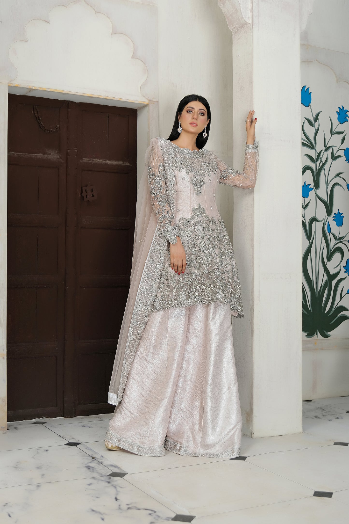 A beautiful blend of soft pink fabric and intricate silver embroidery, creating a striking contrast. The dress is elegantly adorned with silver details that flow seamlessly down the length of the dress, with a matching dupatta that adds an extra layer of grace. Perfect for any formal occasion, this dress is sure to impress with its delicate and eye catching design