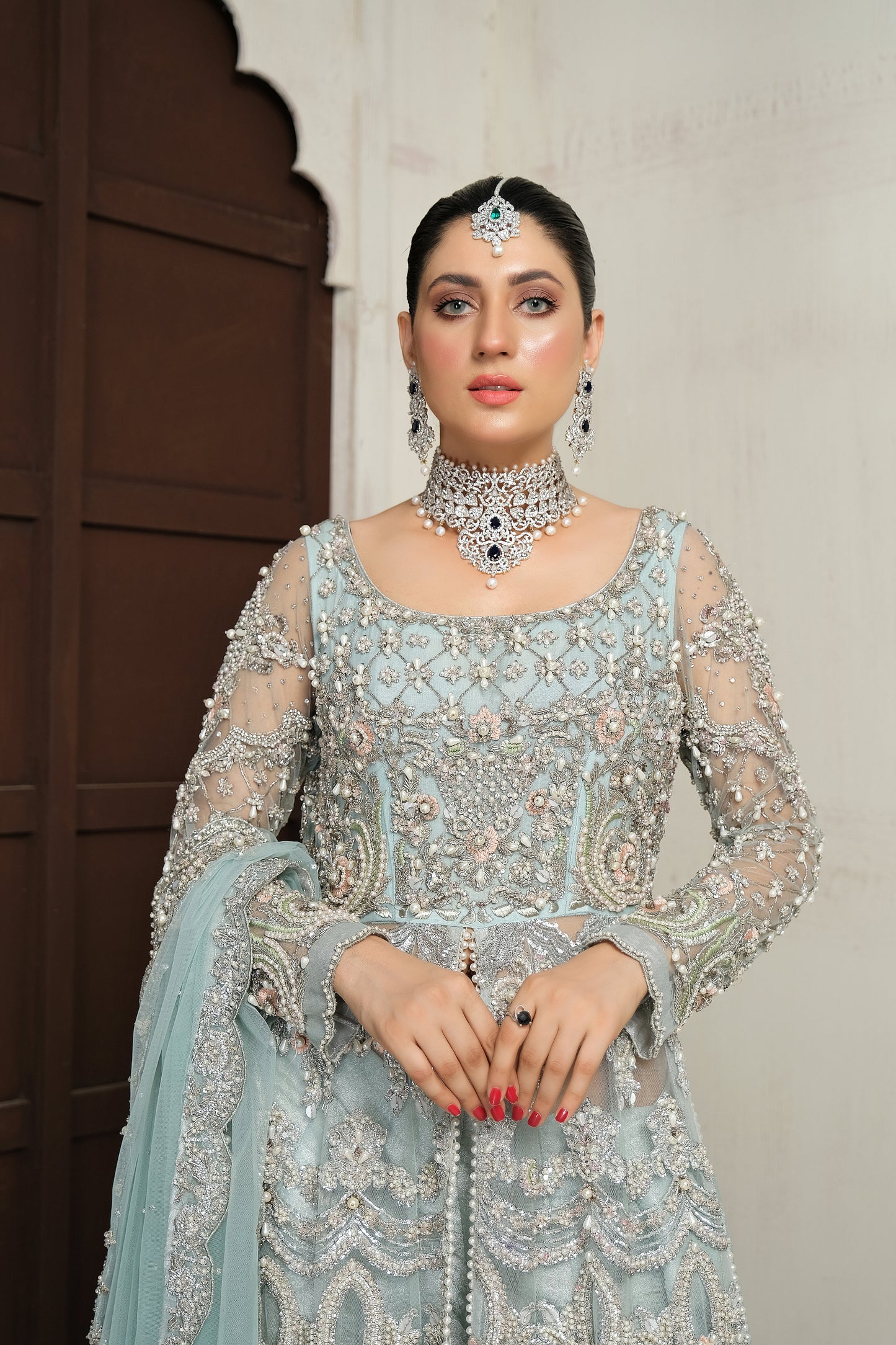 Pakistani ice blue bridal dress with silver work. The dress is a stunning shade of ice blue with intricate silver work embellishments. The neckline and sleeves are adorned with silver embroidery, and the skirt features a heavy silver border. The dress has a flowing silhouette with a fitted bodice and flared skirt. The outfit is completed with a matching dupatta that has a delicate silver border