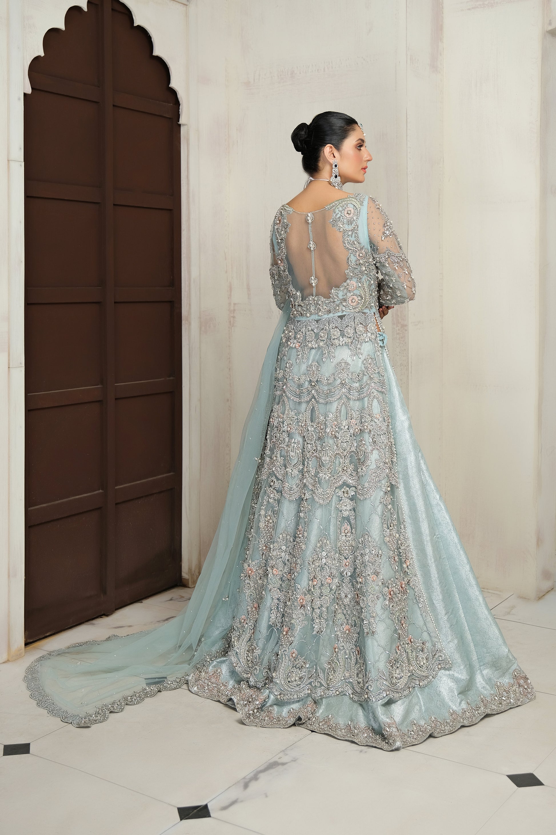 Pakistani ice blue bridal dress with silver work. The dress is a stunning shade of ice blue with intricate silver work embellishments. The neckline and sleeves are adorned with silver embroidery, and the skirt features a heavy silver border. The dress has a flowing silhouette with a fitted bodice and flared skirt. The outfit is completed with a matching dupatta that has a delicate silver border